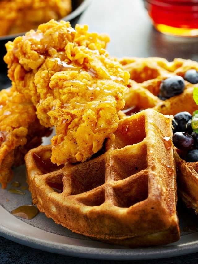 Delicious waffles topped with succulent chicken and juicy blueberries on a plate.