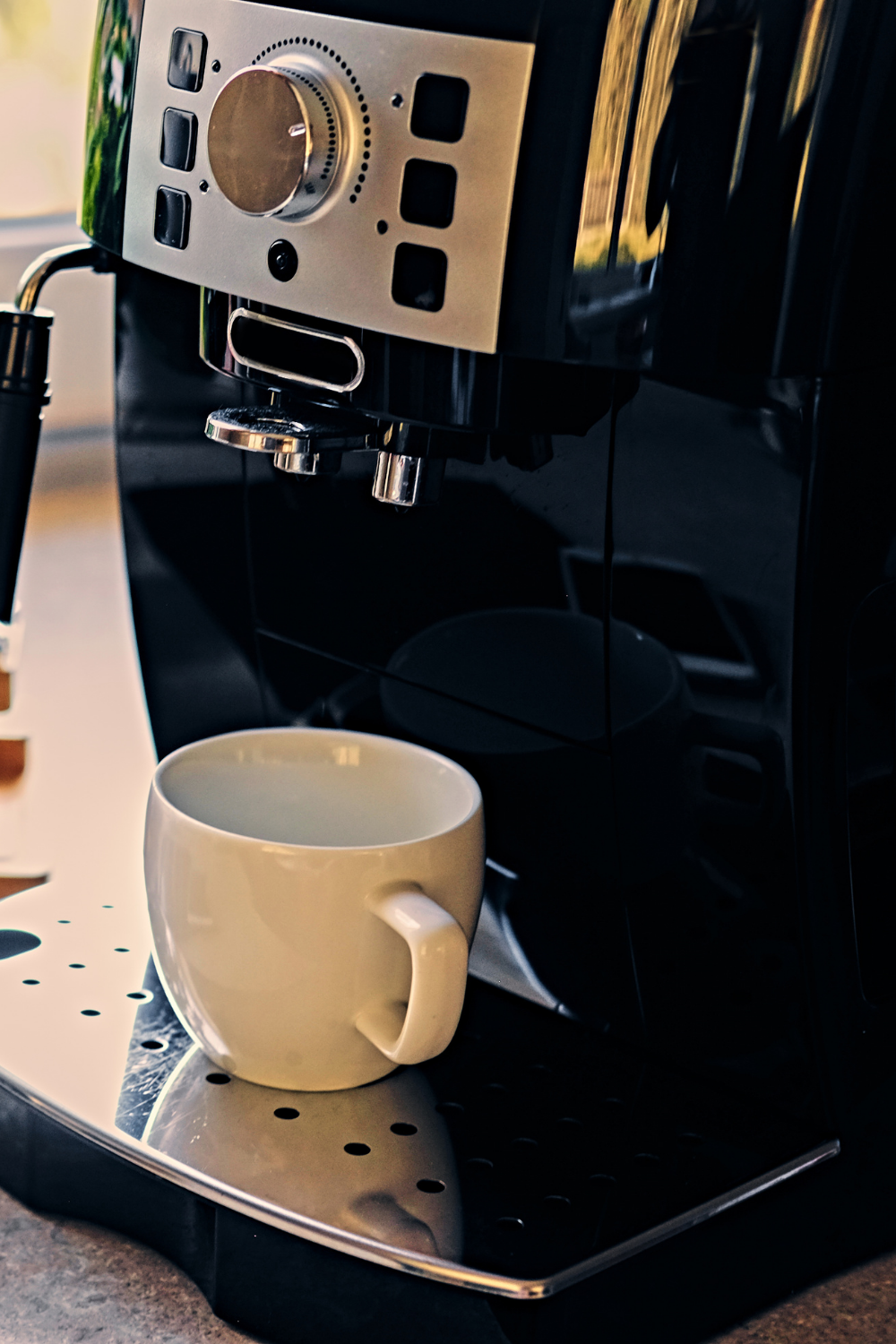 Close-up of a white coffee cup under an espresso machine with sleek metallic and black details.