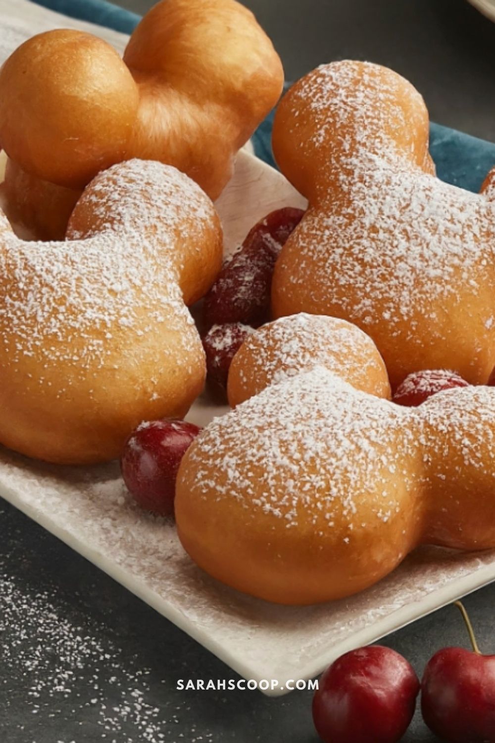 Freshly baked doughnuts dusted with powdered sugar, served with cherries on a white plate.