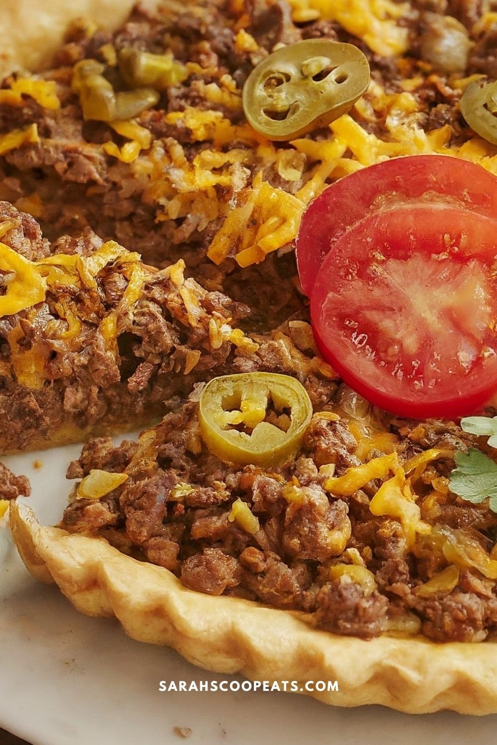 Close-up of a taco pie reminiscent of a Cheeseburger Pie, topped with ground beef, melted cheese, sliced jalapeños, and tomato. The crust is perfectly visible at the bottom.