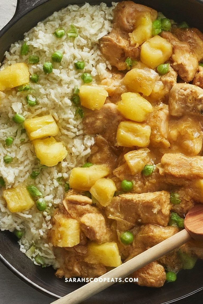 A skillet containing a dish of chicken pieces, pineapple chunks, and peas in a yellow sauce, served alongside white rice.