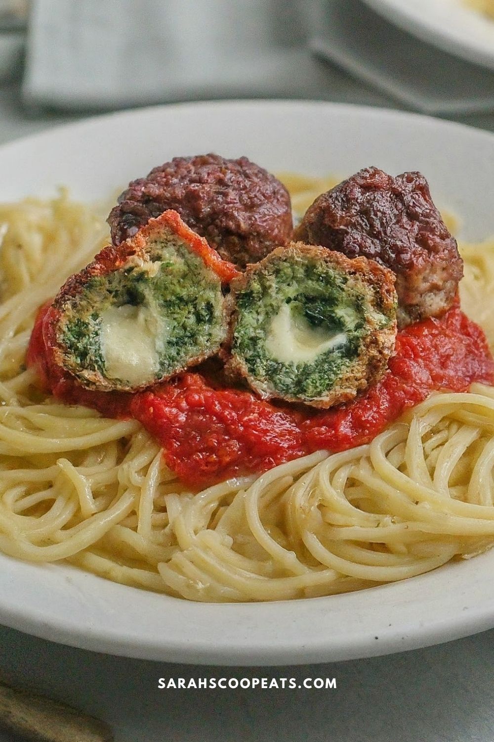A plate of spaghetti with tomato sauce, topped with whole and halved spinach-stuffed meatballs, showing a cheese-filled center.