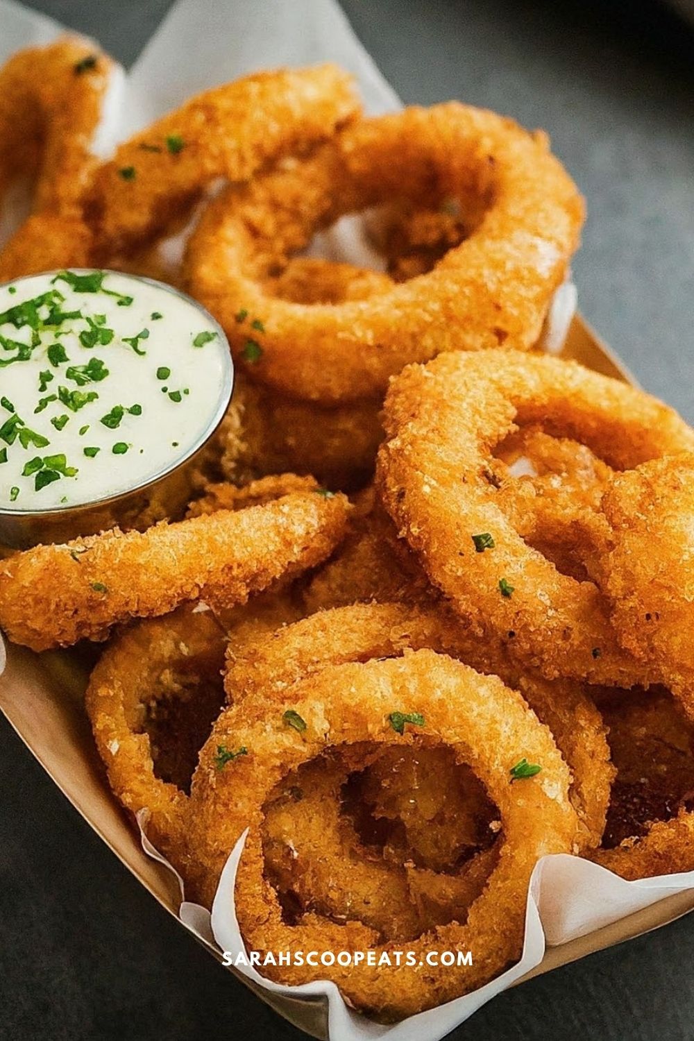 A basket of crispy fried onion rings garnished with chopped chives, served with a side of dipping sauce.