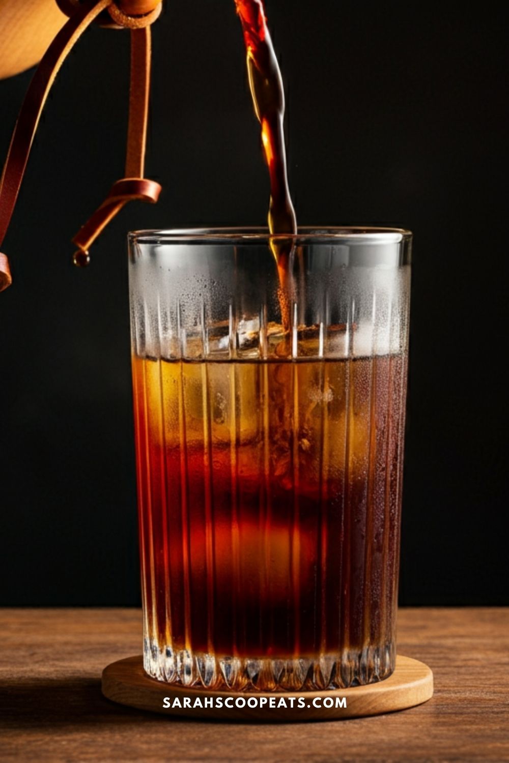 Cold brew coffee, crafted from a Chemex, cascades smoothly into a glass filled with ice on a wooden surface against a dark background.