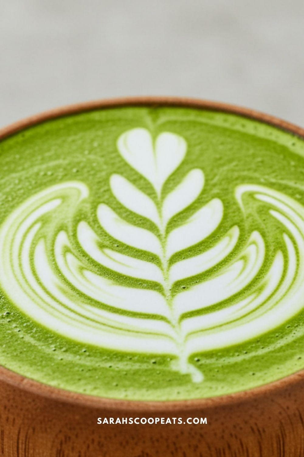 A bowl of matcha latte with intricate leaf-shaped latte art on the surface.