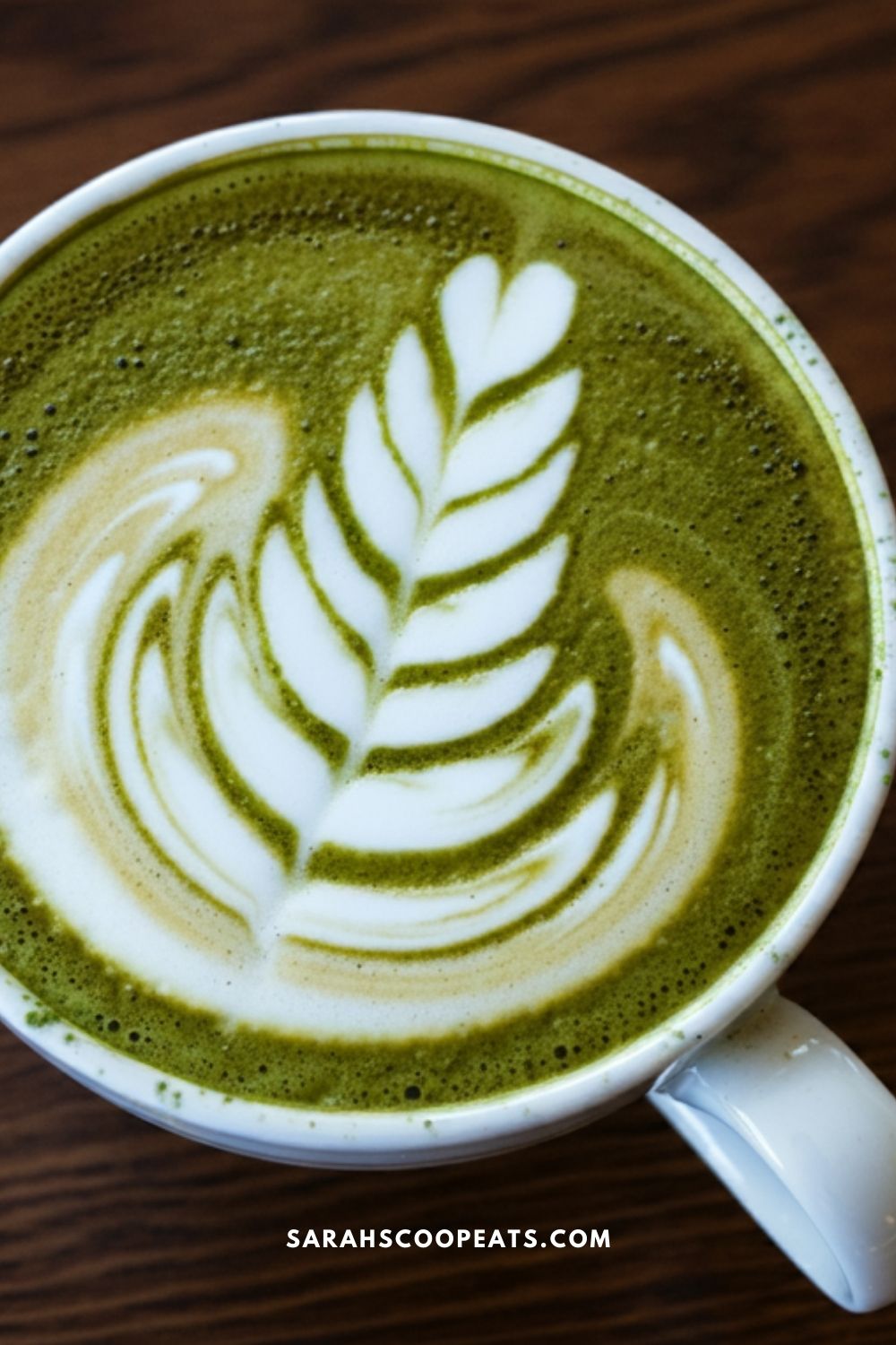 A cup of matcha latte with a leaf design in the foam on a wooden surface.